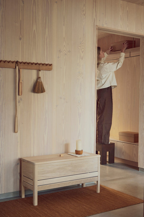 Form & Refine A Line Storage Bench 90, oak storage bench with lid, white oak storage bench beneath a coat rack in a plywood entrance, person hanging a coat