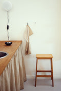 Form & Refine Angle Bar Stool 65, wooden bar stool, oak bar stool at a kitchen counter with a curtained cabinet and a wall lamp