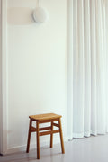 Form & Refine Angle Stool 45, wooden stool, oak stool in a bright room beside sheer curtains and a wall lamp