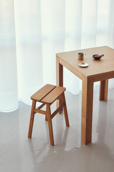 Form & Refine Angle Stool 45, wooden stool, oak stool beside a small oak table in front of sheer curtains