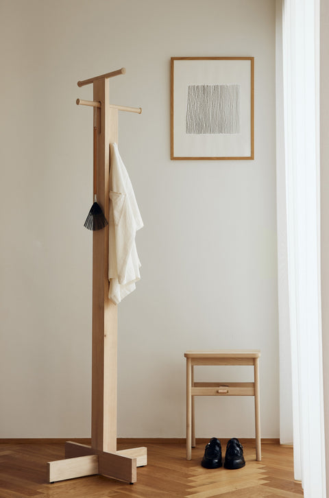 Form & Refine Angle Foldable Stool, folding oak stool, oak foldable stool folded beneath a coat stand by a window, a framed print above