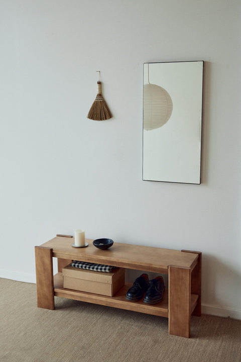 Form & Refine Beam Bench, solid pine bench with shelf, deep brown pine bench with a book and shoes beneath a tall mirror in a hallway