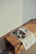Form & Refine Beam Bench, solid pine bench with shelf, newspaper and a cup on the deep brown pine bench, close view