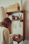 Form & Refine Beam Office Shelf 3, solid pine wall shelf with desk, person writing at the deep brown pine office shelf used as a wall desk