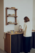 Form & Refine Beam Shelf 3, solid pine wall shelf, deep brown pine wall shelf above a small kitchen counter, person at the sink