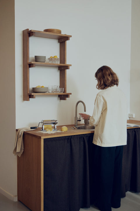 Form & Refine Beam Shelf 3, solid pine wall shelf, deep brown pine wall shelf above a small kitchen counter, person at the sink