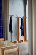Form & Refine Foyer Coat Stand, solid oak coat stand, oak coat stands holding coats beside an oak table in a café with a blue tiled wall