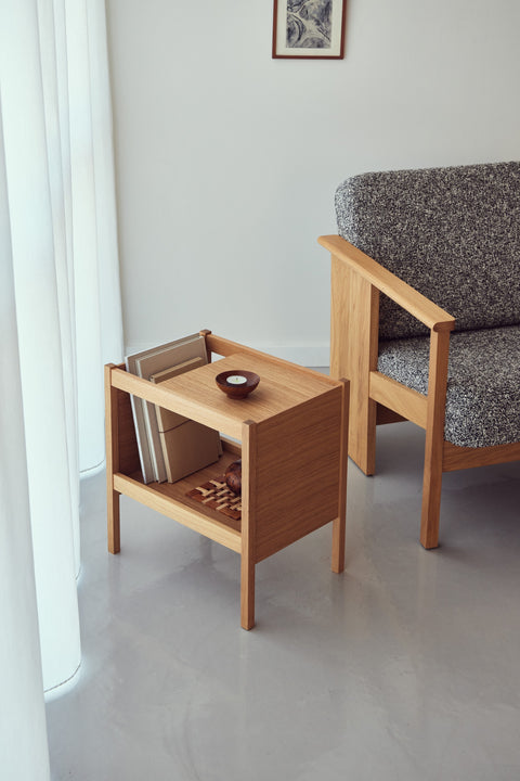 Form & Refine Journal Side Table, solid oak side table with magazine slot, beside a grey armchair with magazines in the slot