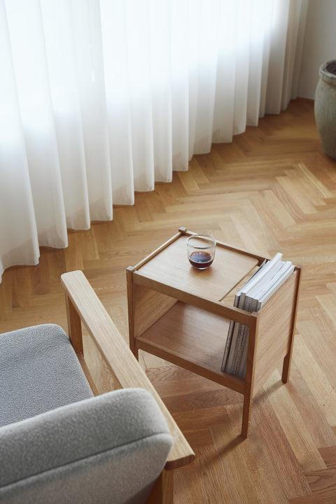 Form & Refine Journal Side Table, solid oak side table with magazine slot, oak side table next to a grey sofa on herringbone parquet, seen from above