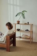 Form & Refine Leaf Shelf 1x3, solid oak shelving unit, child reading in the Icon Lounge Chair beside an oak shelf with a potted fern