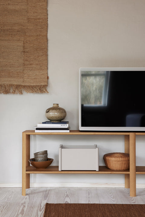Form & Refine Leaf Shelf 2x2, solid oak shelving unit, oak shelf beneath a wall-mounted television holding books, a box and a basket