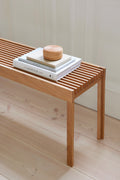 Form & Refine Lightweight Bench, solid oak slatted bench, oak slatted bench with a stack of books and a jar, close view on a pale wood floor