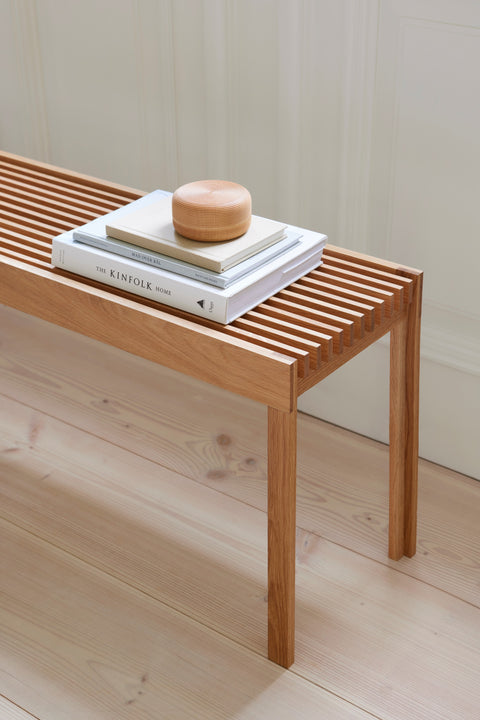 Form & Refine Lightweight Bench, solid oak slatted bench, oak slatted bench with a stack of books and a jar, close view on a pale wood floor