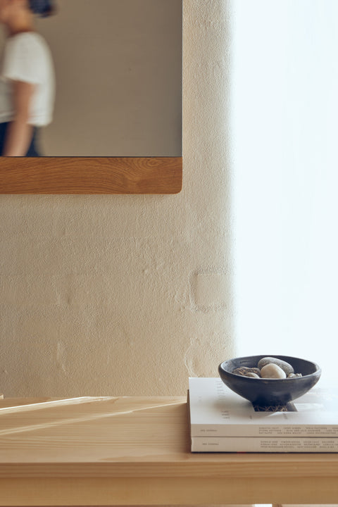 Form & Refine Rim Mirror 35x105, tall oak-framed wall mirror, oak-framed mirror on a whitewashed wall above a bowl on a wooden counter, person passing