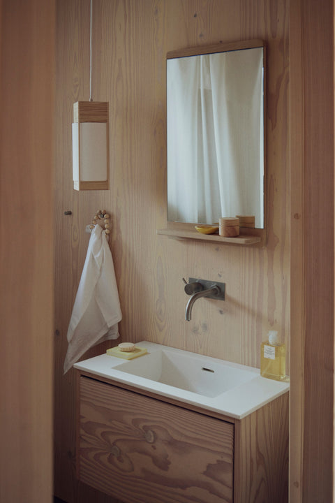Form & Refine Rim Mirror, oak-framed wall mirror with shelf, oak-framed mirror above a basin in a plywood bathroom beside a small wall lamp