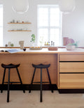 Form & Refine Shoemaker Chair™, No. 68, wooden Shoemaker stool, black Shoemaker stools at a pale oak kitchen island under pendant lamps
