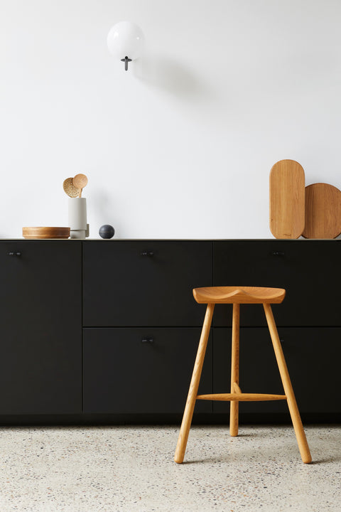 Form & Refine Shoemaker Chair™, No. 68, wooden Shoemaker stool, oak Shoemaker stool at a black kitchen counter with wooden objects on top