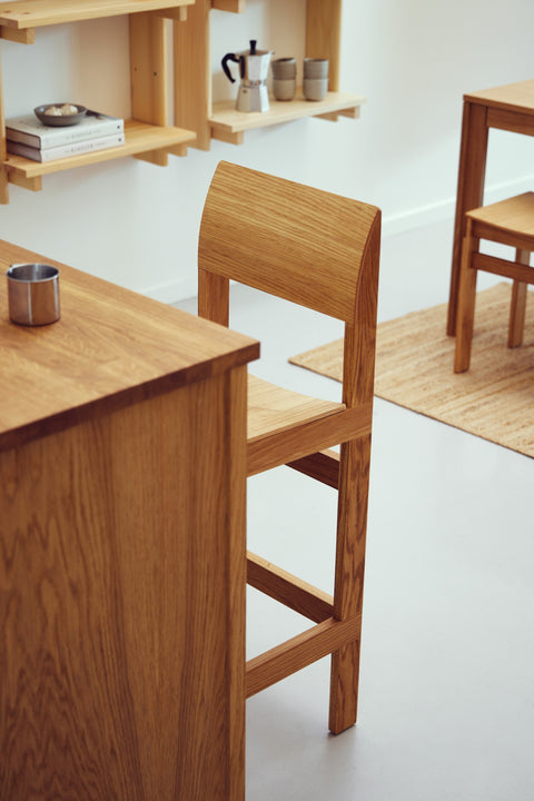 Form & Refine Sonder Bar Chair 65, solid oak bar chair, oak bar chair at a kitchen island beneath a pine wall shelf, seen from behind