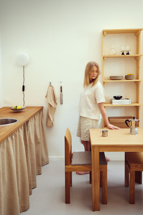 Form & Refine Sonder Chair, solid oak dining chair, person leaning on an oak table with a Sonder chair in a kitchen with open shelves