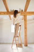 Form & Refine Step by Step Ladder, folding oak ladder, person standing on the oak ladder reaching a beam in a room with timber posts