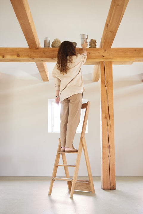 Form & Refine Step by Step Ladder, folding oak ladder, person standing on the oak ladder reaching a beam in a room with timber posts