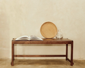 Frama Bench 01 in Dark Brown Birch, dark bench against a plaster wall holding an open book, a round woven tray and a glass carafe