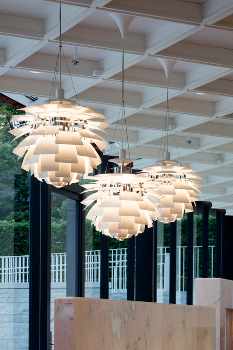 Three white Louis Poulsen PH Artichoke pendants suspended in a bright atrium with grid ceiling and tall windows