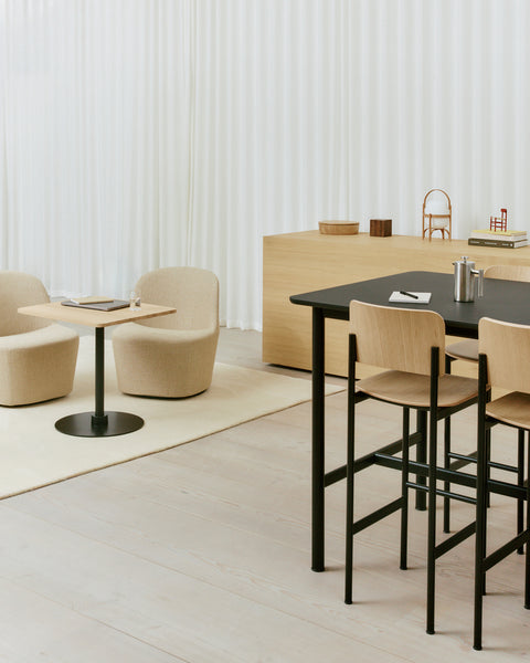 PLAN Barstools with oak seats and black frames around a black high table, styled with lounge chairs in a Scandinavian office.