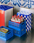 HAY Tin Container, Large, Blue and Off-White, lidded tinplate storage tin, beside blue folding crates of bottles below patterned wall tiles