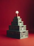 HAY Colour Crate, Small, Sage Green, recycled plastic storage crate, crates and lids stacked into a pyramid with a lamp, on deep red