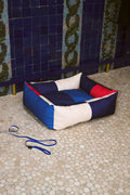 HAY Dog Bed Zip, Medium, Red, Blue, recycled polyester dog bed, on pebbled paving by a blue tiled wall with a striped leash