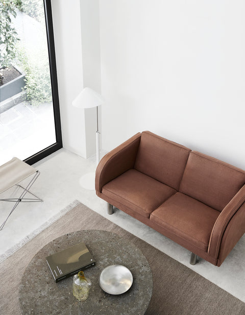 JG Sofa 2 seater in rust fabric with stainless steel legs in minimalist living room beside round stone coffee table