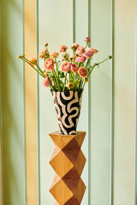 HAY Jessica Hans Shadow Vase, Black and White, patterned ceramic vase with a ruffled rim, holding ranunculus on a wooden plinth by a green wall