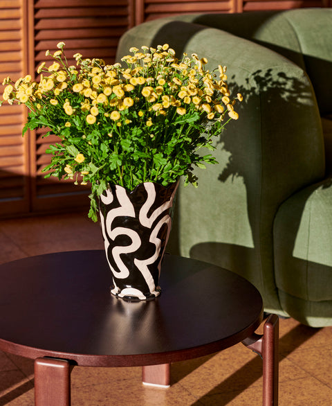HAY Jessica Hans Shadow Vase, Black and White, patterned ceramic vase with a ruffled rim, with yellow daisies on a coffee table by a green sofa