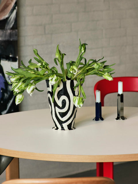 HAY Jessica Hans Shadow Vase, Black and White, patterned ceramic vase with a ruffled rim, with green blooms on a round table beside candleholders