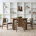 Four Gus* Modern Lanark Dining Chairs in Classic Walnut with Lundy Truffle fabric arranged around round dining table with cork pendant lights and white shelving