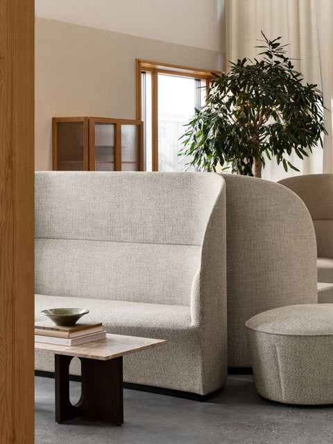 Audo Copenhagen Tearoom Sofa, High Back, light-colored, high-back Tearoom Sofa is shown in a modern living space next to a marble-topped side table and a plant
