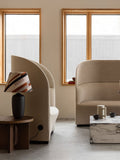 Audo Copenhagen Tearoom Lounge Chair, High Back, side view of the beige Tearoom Lounge Chair, High Back, with its power outlet, in a modern room with a marble coffee table