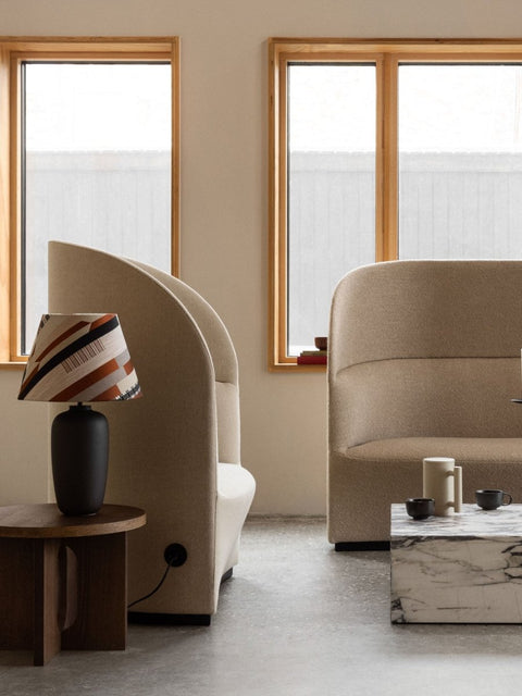 Audo Copenhagen Tearoom Lounge Chair, High Back, side view of the beige Tearoom Lounge Chair, High Back, with its power outlet, in a modern room with a marble coffee table