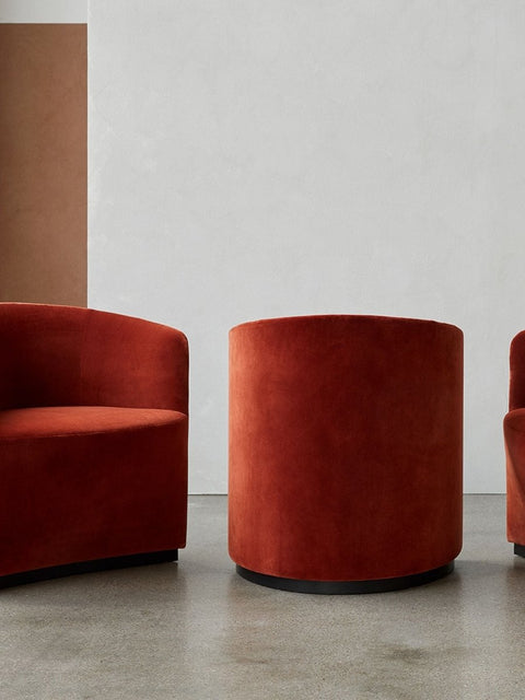 Audo Copenhagen Tearoom Chairs and Sofas, rust-orange velvet Tearoom Club Chair and ottoman are displayed in a minimalist room with a concrete floor and white walls