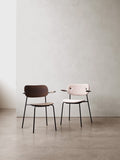 Audo Copenhagen Co Dining Chair, With Arms, Fully Upholstered, Co Dining Chairs with Arms set in a minimalist space. One chair is upholstered in light fabric, the other in dark wood