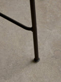 Audo Copenhagen Co Bar Chair, Non-Upholstered, close-up shot of the Co Bar Chair's black powder-coated steel leg and footrest joint, shown on a grey concrete floor