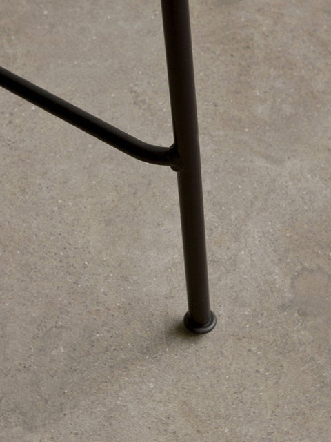 Audo Copenhagen Co Bar Chair, Non-Upholstered, close-up shot of the Co Bar Chair's black powder-coated steel leg and footrest joint, shown on a grey concrete floor