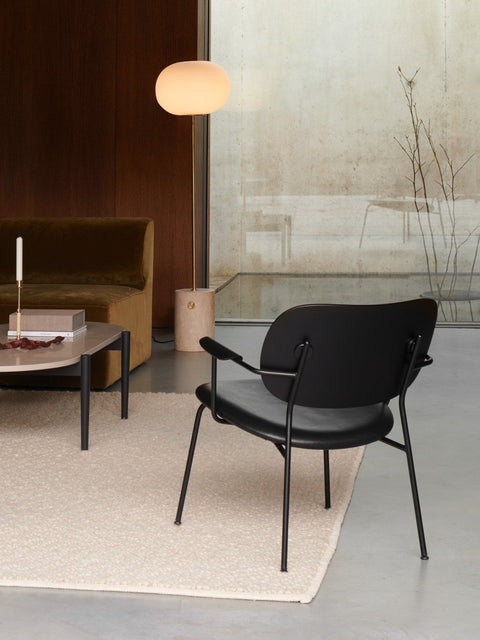 Audo Copenhagen Co Lounge Chair, Partially Upholstered, black Co Lounge Chair on a cream rug in a modern living room, with a brown sofa, coffee table, and floor lamp nearby