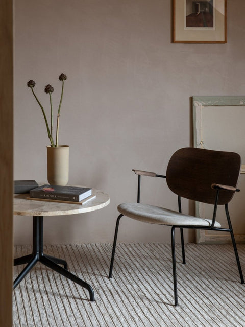 Audo Copenhagen Co Lounge Chair, Partially Upholstered, dark wood Co Lounge Chair with a light seat stands next to a marble-topped Harbour Column Table on a textured Gravel Rug