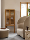Audo Copenhagen Tearoom Lounge Chair, High Back, beige Tearoom Lounge Chair in a lounge with a Cairn Pouf, a marble Plint, a Column Lamp, and a Curiosity Cabinet