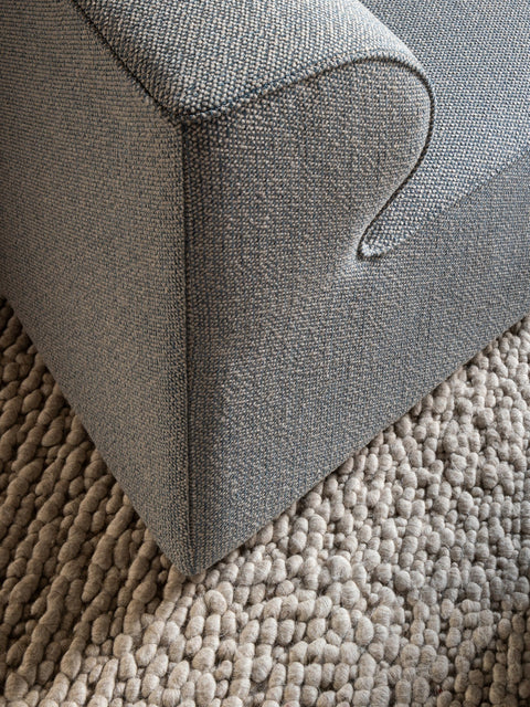 Corner detail of Eave Modular Sofa in grey fabric with curved armrest on wool rug