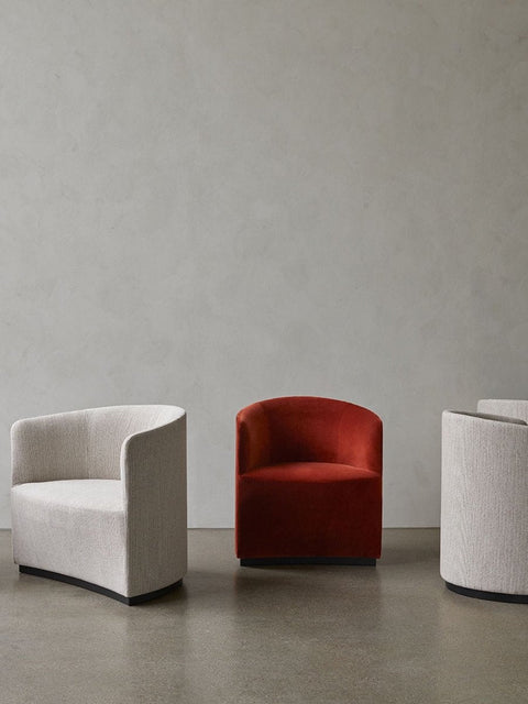 Audo Copenhagen Tearoom Swivel Chair, With Return, Tearoom Chairs are displayed against a neutral grey wall and floor. One chair is upholstered in burnt orange velvet