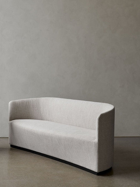 Audo Copenhagen Tearoom Chairs and Sofas, three-quarter view of the Tearoom Sofa in a cream fabric, featuring a sculptural curved back and a recessed black base