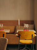 Audo Copenhagen Co Dining Chair, With Arms, Fully Upholstered, yellow, fully upholstered Co Dining Chair with arms in a restaurant, with an Umanoff Candle Holder on a marble table